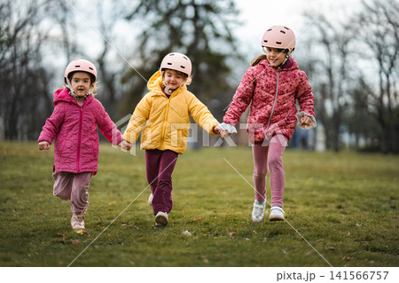 Three young girls running together holding hands in park Three young girls running together holding hands in park 141566757