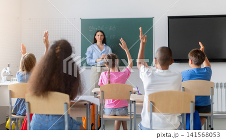 Diverse students raising their hands to answer female teacher during mathematics lesson 141568053