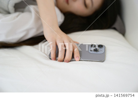 スマホのアラームを止める寝起きの20代日本人女性 スマホのアラームを止める寝起きの20代日本人女性 141569754