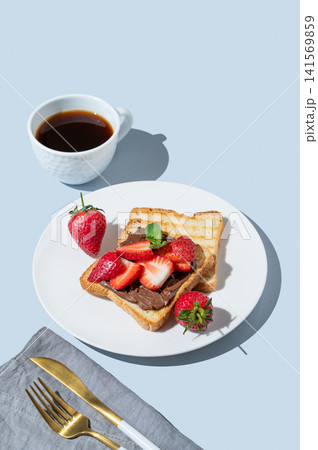 Toasted bread with chocolate cream and strawberry on a white plate on a blue background Toasted bread with chocolate cream and strawberry on a white plate on a blue background 141569859