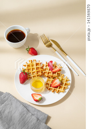 Belgian waffles with fresh strawberries and honey on a white plate on a yellow background Belgian waffles with fresh strawberries and honey on a white plate on a yellow background 141569870