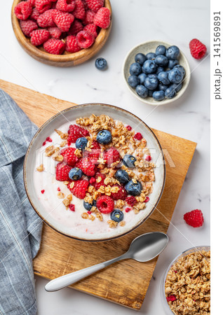 Natural greek yogurt with granola, blueberry and raspberry in a bowl on a wooden board Natural greek yogurt with granola, blueberry and raspberry in a bowl on a wooden board 141569891