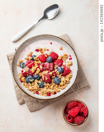 Natural greek yogurt with granola, blueberry and raspberry in a bowl on a light textured background Natural greek yogurt with granola, blueberry and raspberry in a bowl on a light textured background 141569892