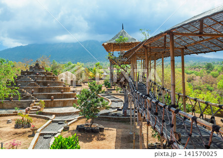 Bamboo treehouse and stone buddhist stupa in Tulamben, Bali, Indonesia with scenic mountain view of Agung volcano and tropical greenery. Sustainable architecture and rural adventure tourism location. 141570025