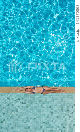 Young woman relax at the edge of clear blue pool during sunny summer vacation. This aerial view captures family, friends, fun, and recreation at resort, relaxation and joyful outdoor moments. Young woman relax at the edge of clear blue pool during sunny summer vacation. This aerial view captures family, friends, fun, and recreation at resort, relaxation and joyful outdoor moments. 141570062