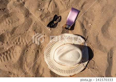 Flat Lay of Summer Sun Protection Essentials Straw Hat Sunglasses and Cream Tube on Sand Flat Lay of Summer Sun Protection Essentials Straw Hat Sunglasses and Cream Tube on Sand 141570333