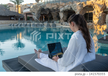Side View of Woman Checking Financial Dashboard on Tablet near Resort Pool Caves Side View of Woman Checking Financial Dashboard on Tablet near Resort Pool Caves 141570355