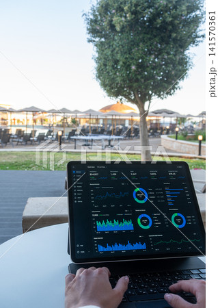Hands Typing on Tablet with Financial Dashboard at Resort Outdoor Terrace Hands Typing on Tablet with Financial Dashboard at Resort Outdoor Terrace 141570361