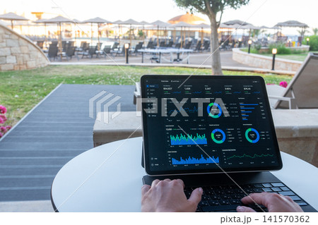 Hands Typing on Tablet with Financial Dashboard at Resort Outdoor Terrace Hands Typing on Tablet with Financial Dashboard at Resort Outdoor Terrace 141570362