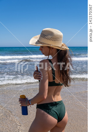 Young Woman Applying Sunscreen on Shoulder at Sandy Beach Near Sea Young Woman Applying Sunscreen on Shoulder at Sandy Beach Near Sea 141570367