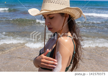 Close Up of Young Woman Applying Sunscreen Lotion on Her Shoulder at Beach Close Up of Young Woman Applying Sunscreen Lotion on Her Shoulder at Beach 141570373