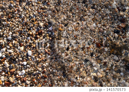 Clear sea water wave washing over colorful small beach pebbles 141570573