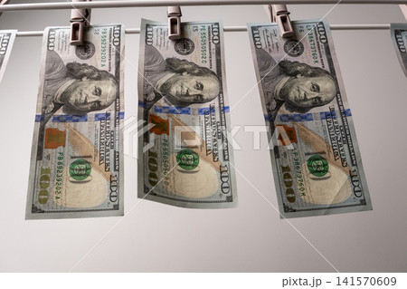 One hundred dollar bills hanging on clothesline with plastic pins One hundred dollar bills hanging on clothesline with plastic pins 141570609