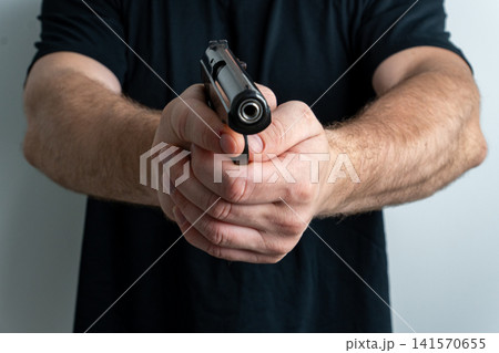 Man holding black handgun aimed directly at camera on plain background Man holding black handgun aimed directly at camera on plain background 141570655