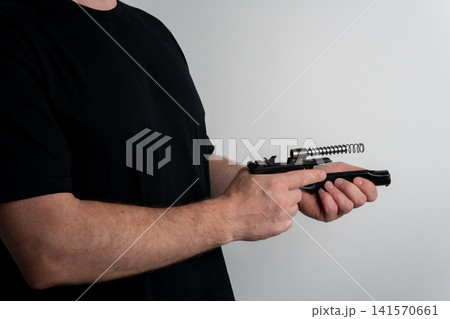 Man disassembling semi automatic pistol for maintenance on plain background Man disassembling semi automatic pistol for maintenance on plain background 141570661