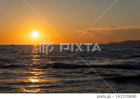 Bright golden sunset over calm sea water surface with distant boat Bright golden sunset over calm sea water surface with distant boat 141570690