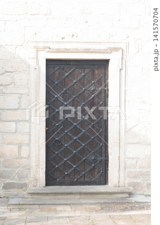 Ancient wooden door with forged iron grill decoration in stone wall Ancient wooden door with forged iron grill decoration in stone wall 141570704