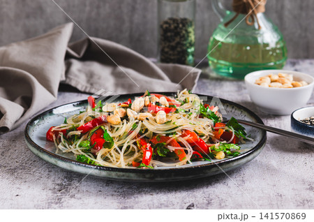 A delicious salad of glass noodles, fried bell peppers, cilantro, and nuts on a plate on the table A delicious salad of glass noodles, fried bell peppers, cilantro, and nuts on a plate on the table 141570869