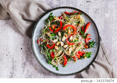 Close up of a delicious salad of glass noodles, fried bell peppers, cilantro, and nuts on a plate on the table top view Close up of a delicious salad of glass noodles, fried bell peppers, cilantro, and nuts on a plate on the table top view 141570874