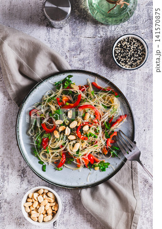 Rice noodles funchose with bell pepper, herbs and peanuts on a plate on the table top and vertical view Rice noodles funchose with bell pepper, herbs and peanuts on a plate on the table top and vertical view 141570875