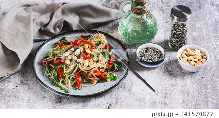 A delicious salad of glass noodles, fried bell peppers, cilantro, and nuts on a plate on the table web banner 141570877