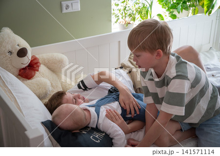 Three brothers spend quiet family time together on bed in cozy children bedroom while older sibling gently plays with younger boys. Family, sibling bond, parenting, childhood, home lifestyle Three brothers spend quiet family time together on bed in cozy children bedroom while older sibling gently plays with younger boys. Family, sibling bond, parenting, childhood, home lifestyle 141571114