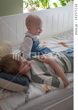 Baby sits beside older brother on bed during quiet family moment in cozy childrens bedroom at home. Family, sibling bond, childhood, parenting, home lifestyle, comfort, togetherness, care Baby sits beside older brother on bed during quiet family moment in cozy childrens bedroom at home. Family, sibling bond, childhood, parenting, home lifestyle, comfort, togetherness, care 141571116