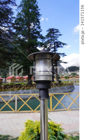 Close-up of ornate black metal lamp post with a yellow metal railing and red-roofed cabins, tourism concept. Close-up of ornate black metal lamp post with a yellow metal railing and red-roofed cabins, tourism concept. 141571156