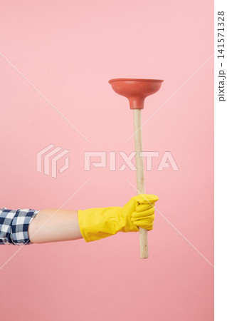 Person's gloved hand extending across a pink background, holding a household plunger, symbolizing cleaning, plumbing, solution, and readiness for tasks 141571328