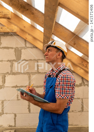 Construction worker or engineer inspecting a residential roof structure and unfinished building interior, writing notes regarding the build process and project development 141571406