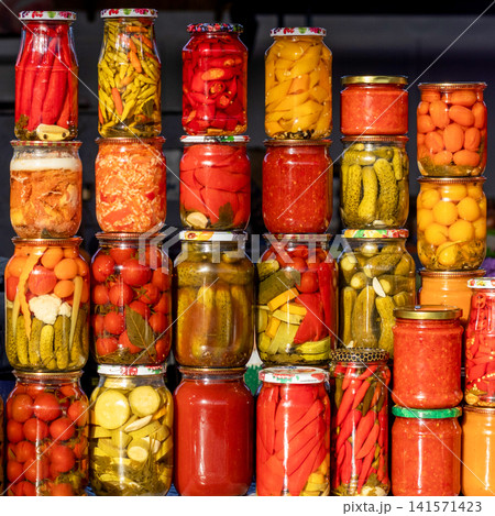 Colorful homemade pickled vegetables in glass jars stacked for sale at a market or pantry display Colorful homemade pickled vegetables in glass jars stacked for sale at a market or pantry display 141571423
