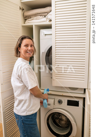 Middle aged woman pouring detergent into washing machine Middle aged woman pouring detergent into washing machine 141571648