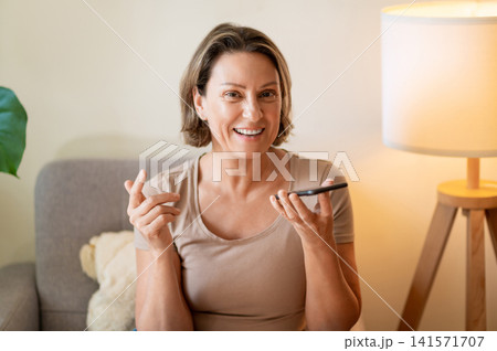 Laughing middle aged woman dictating voice message to phone Laughing middle aged woman dictating voice message to phone 141571707