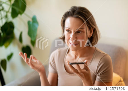 Pensive middle aged female recording audio message on phone Pensive middle aged female recording audio message on phone 141571708