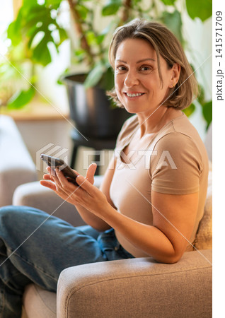Happy middle aged woman looking at camera with smartphone Happy middle aged woman looking at camera with smartphone 141571709