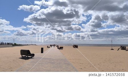 wide sandy beach with a paved promenade leading towards the ocean under a blue sky with fluffy white clouds wide sandy beach with a paved promenade leading towards the ocean under a blue sky with fluffy white clouds 141572038