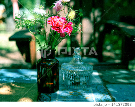 Fresh colorful wildflowers arranged in a vintage amber glass bottle on a rustic outdoor table. Sun-dappled garden still life with natural light, nostalgic atmosphere and shallow depth of field. Fresh colorful wildflowers arranged in a vintage amber glass bottle on a rustic outdoor table. Sun-dappled garden still life with natural light, nostalgic atmosphere and shallow depth of field. 141572098