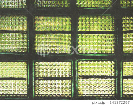 Close-up of a vintage textured green glass window illuminated by soft green daylight. Geometric glass pattern creates an abstract architectural background with retro character and rich texture. 141572297