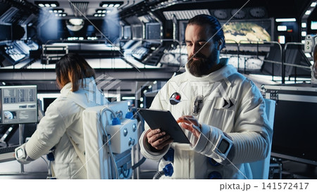 Astronaut checking human expansion in space mission data on tablet during journey to Mars. Cosmonaut in starship prepares for red planet expedition supporting long term mankind survival 141572417