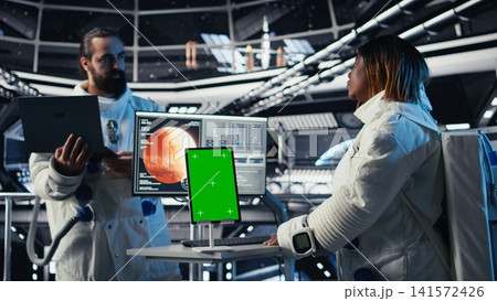 Astronauts reviewing onboard analytics on isolated screen tablet before stepping outside starship. Cosmonauts verifying parameters on chroma key device after landing on planet 141572426