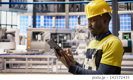 Industrial plant technician using tablet to implement green energy solutions, integrating solar tech in assembly systems. Smart factory worker enhancing production efficiency using device, camera A 141572435