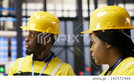 Manager overseeing work done by engineer in smart factory, ensuring quality control during manufacturing. Team leader supervising employee monitoring automated conveyor systems, camera B Manager overseeing work done by engineer in smart factory, ensuring quality control during manufacturing. Team leader supervising employee monitoring automated conveyor systems, camera B 141572468