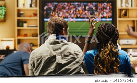 Football supporters at home argue over referee decision, shouting and raising hands during tense match. Soccer fans show frustration through frantic gestures, reacting to dramatic live game on TV 141572548