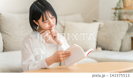リビングで本を読みながら悩む,考える,困る中学生,高校生の女の子 リビングで本を読みながら悩む,考える,困る中学生,高校生の女の子 141575513