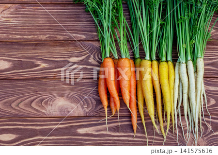 Yellow, orange and white carrots on the brown wooden table. Yellow, orange and white carrots on the brown wooden table. 141575616
