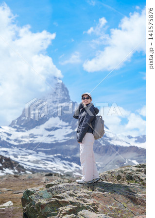 Woman Tourist Exploring Zermatt, Switzerland in summer. Happy Hiker Standing on Rock along Hiking Trail with Matterhorn, Swiss Alps, Famous Europe Landmark, Hiking Attraction and Travel Destination 141575876