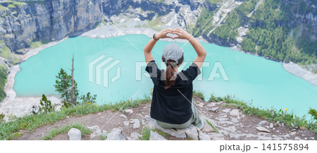 Woman Tourist Explore Oeschinensee, Kandersteg, Switzerland in Summer. Hiker Making Heart Shape at Turquoise Alpine Lake and Hiking Trail View, Popular Europe Tourist Attraction and Travel Destination 141575894