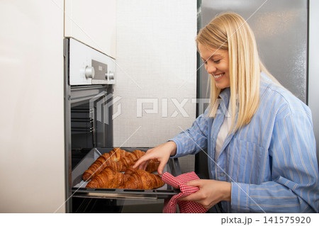 Baking. Woman removes golden croissants from oven in modern kitchen. Baking concept 141575920
