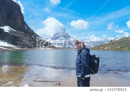 man Tourist Exploring Zermatt, Switzerland. happy hiker sightseeing iconic Matterhorn Swiss Alps at Riffelsee Lake, Famous European Landmark, Hiking Attraction and Travel Destination in Europe 141576015