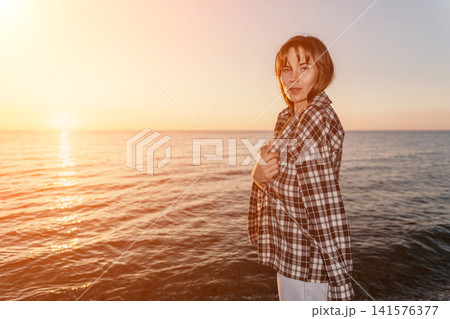 Sunset woman beach standing near the peaceful ocean during golden hour wearing a casual plaid shirt with copy space 141576377